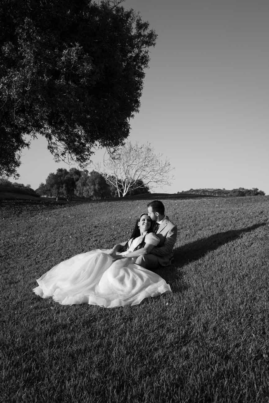 Bride and groom sitting together on a grassy field, in black and white