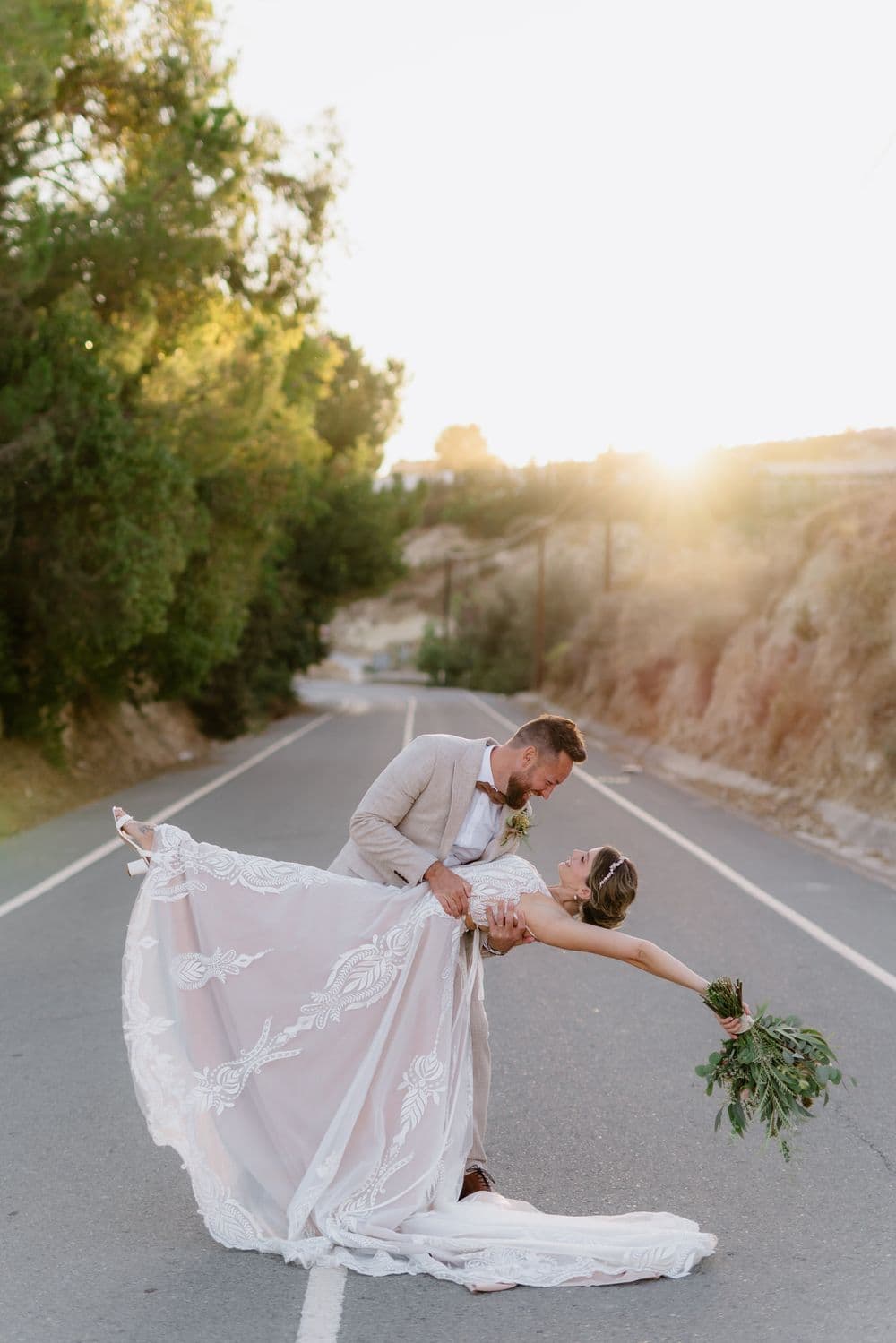 Groom dips his bride for a kiss on a quiet road at sunset