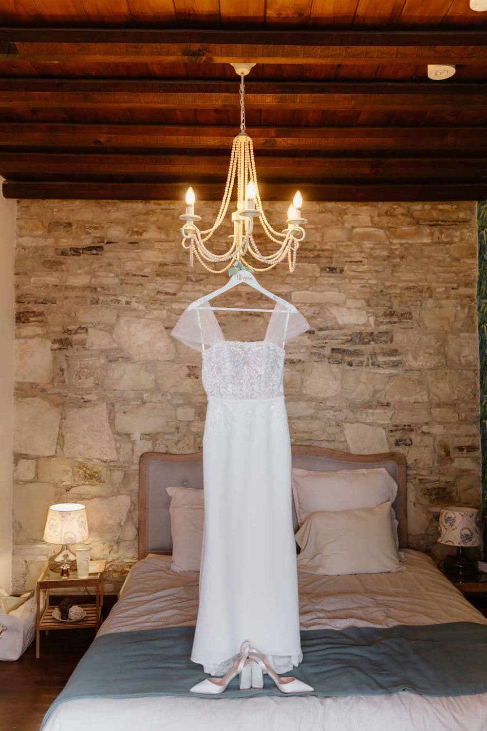 White wedding dress displayed on a hanger beneath an elegant chandelier in a rustic bedroo