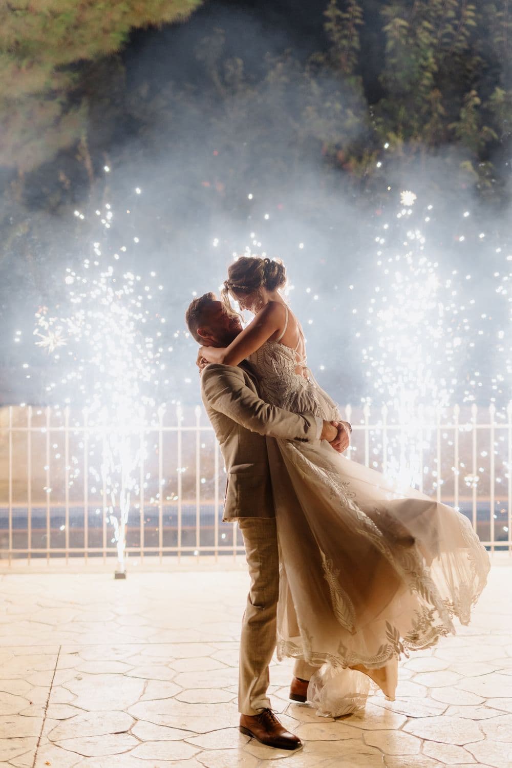 A couple embraces during their first dance with sparklers creating a magical backdrop.