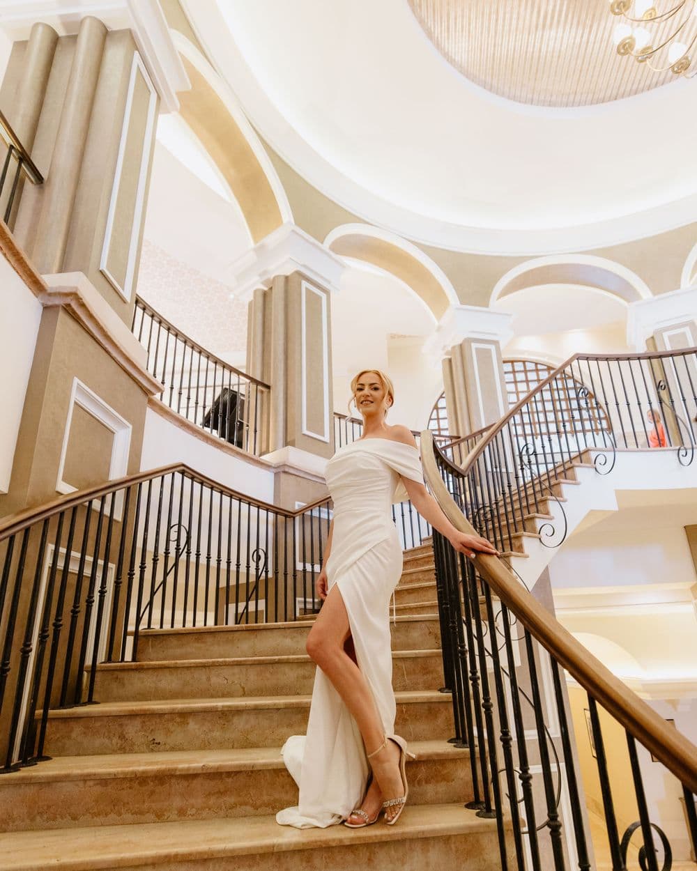 Elegant bride poses on the grand staircase of Elysium Hotel in Paphos, radiating style and