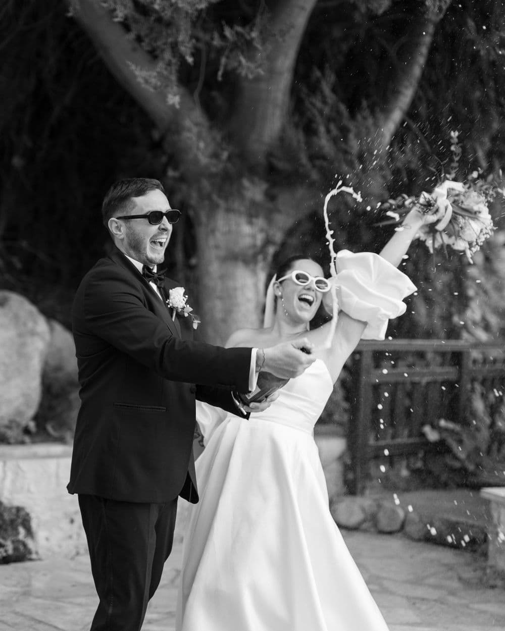 Joyful newlyweds celebrate with champagne spray during outdoor wedding photoshoot in black