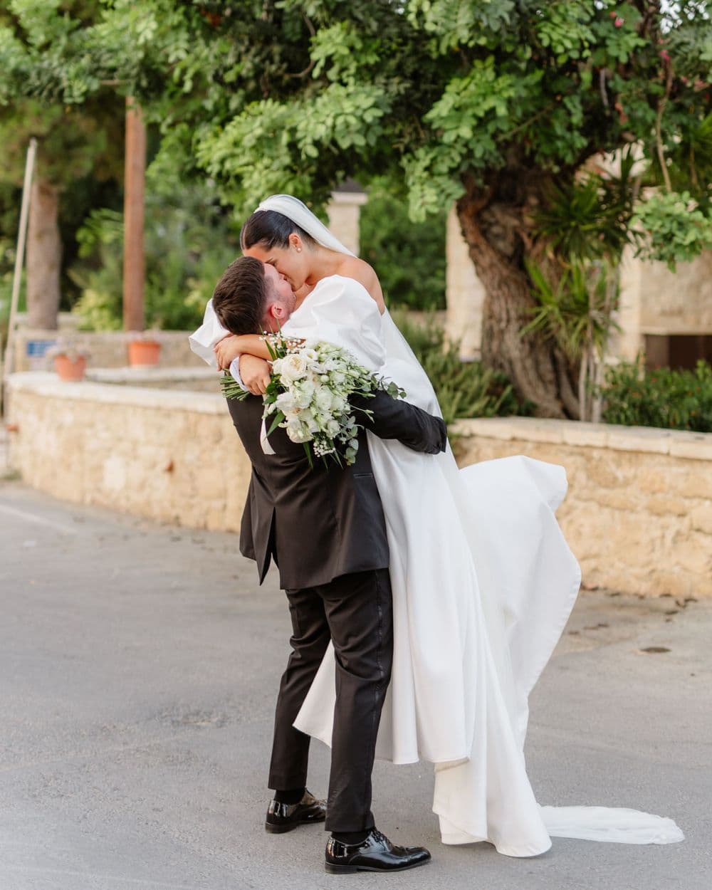 Loving embrace between newlyweds on stone pathway surrounded by greenery.