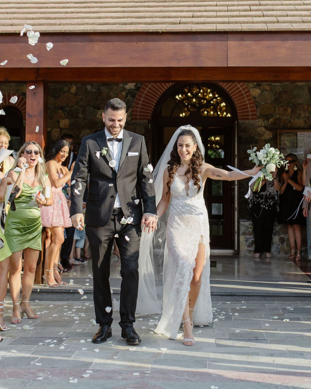 Jubilant newlyweds exit ceremony as guests throw flower petals in celebration.