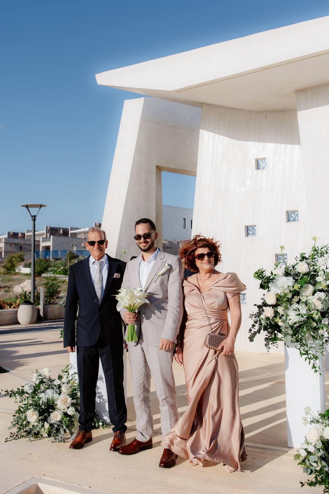 Christos & Eleni, the bride with her parents in front of the chapel