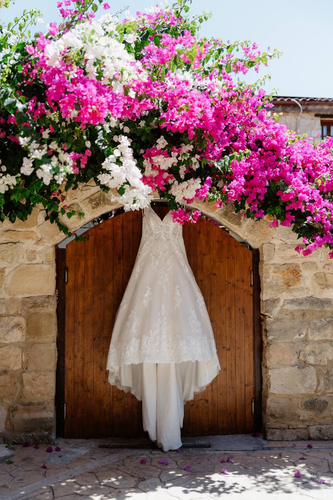 Rita & Andrej, the wedding dress hanging on an old wooden door under bougainvillea